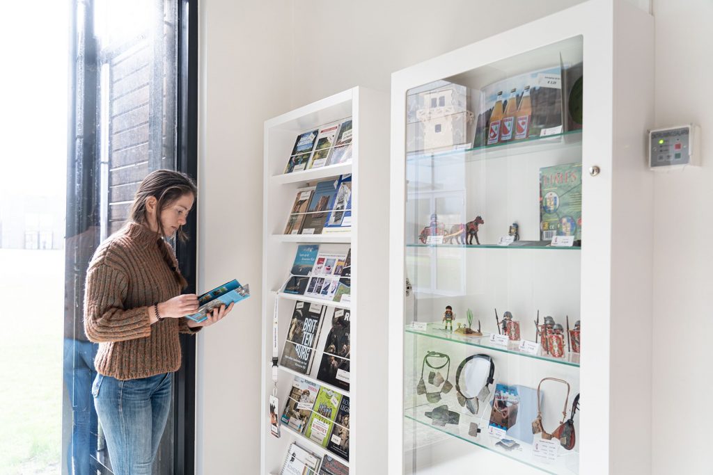 Een vrouw staat naast de glazen vitrines van de museumwinkel en leest een folder.