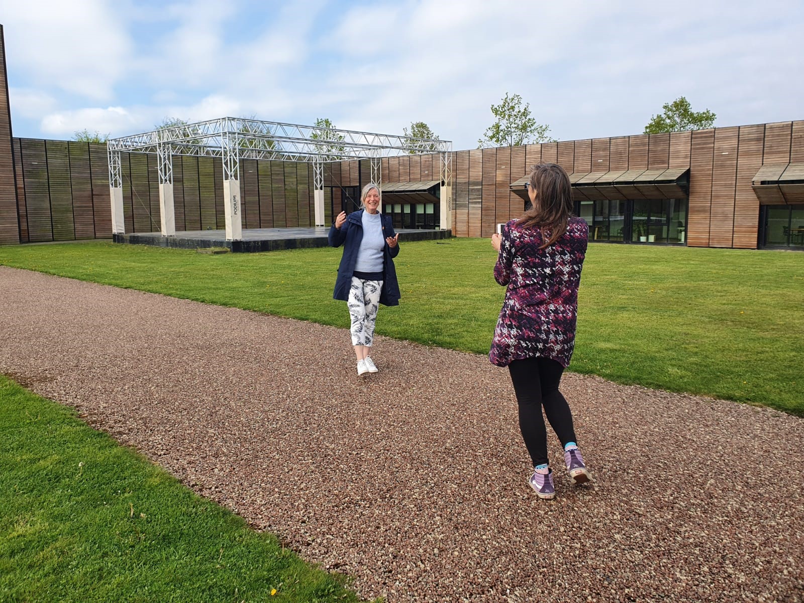Opname-castellum-hoge-woerd-vlog-museum-verhalen-video-binnenplaats-romeinse-weg Een vrouwelijke medewerker van het Castellum staat op de Romeinse weg in de binnenplaats, terwijl zij uitbundig vertelt. Een vrouwelijke fotograaf filmt haar.